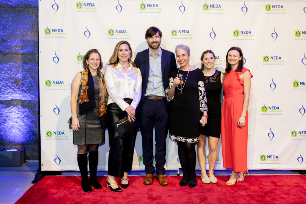 A group of people in formal clothes standing in front of a step and repeat.